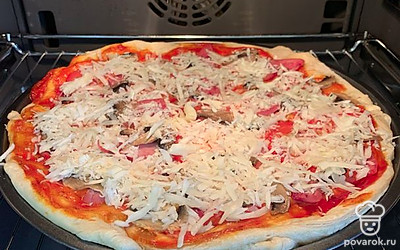 Через 30 минут после начала выпечки достать пиццу и посыпать тертым сыром. Оставить в духовке ещё на 5 минут. И пицца готова.