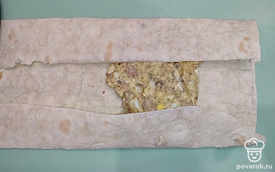 Разрежьте тонкий лаваш на прямоугольники. Ближе к центру выложите начинку. Загните две противоположные стороны лаваша к центру. Начните сворачивать лаваш снизу вверх, образуя небольшой прямоугольник-конвертик.