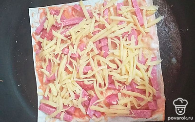 Выложить кусочки колбасы на поверхность лаваша, сверху присыпать тертым сыром. Жарить на сухой разогретой сковороде 3-5 минут под крышкой до полного расплавления сыра.