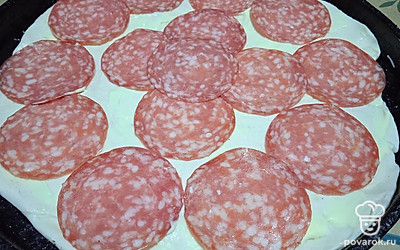 Смажьте сырным соусом и разложите нарезанную сырокопченую колбасу.