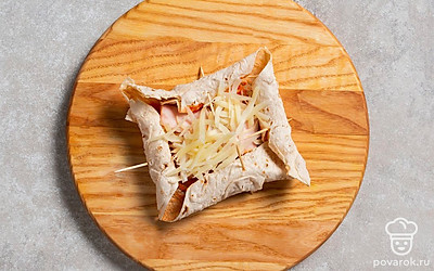 Смажьте лаваш кетчупом, сверху посыпьте частью тертого сыра. Распределите кусочки ветчины, а поверх снова высыпьте тертый сыр. 