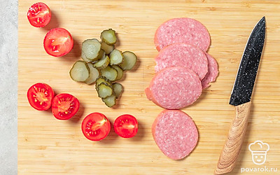 Колбасу и огурец нарежьте кружочками. Помидоры черри разрежьте пополам. Если вы взяли крупные помидоры, то нарежьте их кольцами.