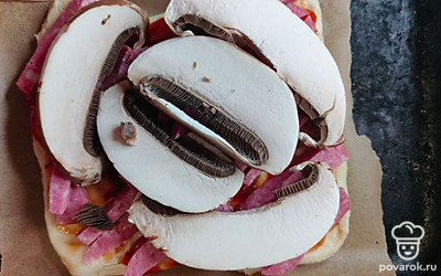 Нарежьте тонкими слайсами грибы и выложите на сервелат. 