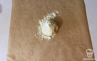 На пергаментную бумагу выложите тесто и присыпьте его мукой.