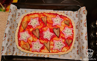 Тесто смазываем кетчупом, делаем рисунок из колбасы и огурцов. В звезды кладем начинку с луком и огурцами.