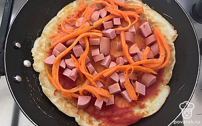 Далее основу для пиццы смажьте томатной пастой. Поверх выложите сосиску и корейскую морковь.