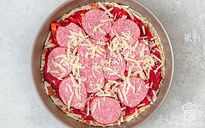 Сверху положите второй круг лаваша и смажьте его томатным соусом. Нарежьте слайсами колбасу и положите на основу пиццы. Тонко нашинкуйте перец и лук, разложите поверх колбасы и натрите сверху оставшийся сыр. Выпекайте не дольше семи минут.