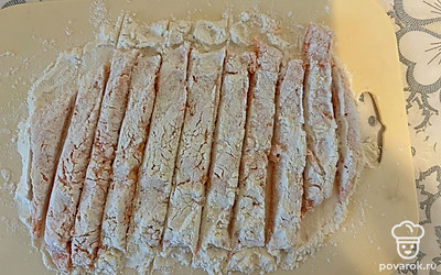 На доску выложите тесто. Посыпьте его одной ложкой муки. Слегка раскатайте тесто и разрежьте на палочки. 