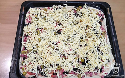 Выложите начинку слоями: сервелат, помидоры, оливки, маслины, сыр. Поставьте пиццу в разогретую до 180 градусов духовку на 15-20 минут на верхнюю полку.