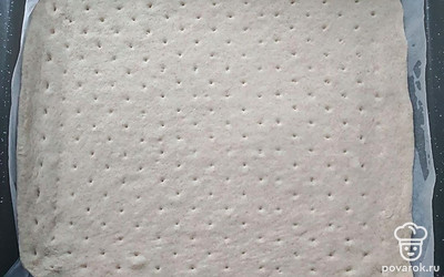 Затем раскатайте тесто в прямоугольный пласт. Подготовьте противень и застелите на него пергамент. Намотайте тесто на скалку и переложите на противень. Выровняйте тесто и проколите вилкой всю поверхность теста.