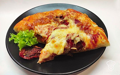 Пиццу разрежьте на треугольные секторы и подайте порционно. Украсьте листовой салатной зеленью. Положите кусочек вяленого помидора.