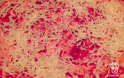 Приступите к выкладыванию начинки. Равномерно распределите томатный соус по поверхности коржа. Посыпьте частью тертого сыра.