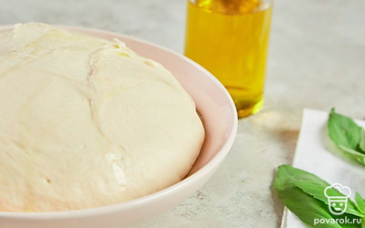 Замесите тесто для пиццы. Смешайте в воде сухие дрожжи и сахар, оставьте смесь в теплом месте на 15 минут. Затем начните засыпать порционно муку, вымешивая пышное рыхлое тесто. В середине замеса добавьте оливковое масло и соль. Дайте тесту подойти около 30 минут.