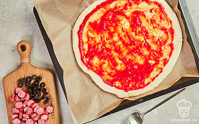 Сделайте основу для пиццы. Присыпьте стол мукой и, не сильно прижимая скалкой, раскатайте его в лепешку. Подождите 10 минут и, если тесто продолжит подниматься, еще немного раскатайте. Выложите лепешку на противень и смажьте ее томатным соусом.