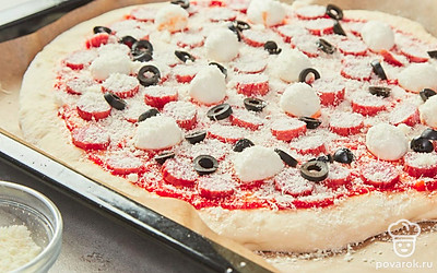 Добавьте начинку и приготовьте пиццу. Равномерно распределите на соусе кружочки сыра моцарелла, поверх них разложите кусочки колбасок и колечки маслин. Посыпьте тертым сыром пармезан. Поставьте пиццу в духовку и выпекайте 10-15 минут.