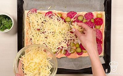 Соберите пиццу. Каждый кусочек теста смажьте смесью майонеза с кетчупом. Посыпьте соус приправой для курицы. Разложите на тесте с соусом колбасную соломку и распределите по ней полукольца лука. Равномерно положите кружочки маринованных огурцов и соленых помидоров. Посыпьте тертым сыром.