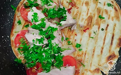 Следом разложите кружочки помидоров, ломтики буженины. Присыпьте зеленью и закройте лепешку второй половиной.