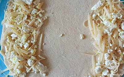 Раскатайте тесто в круг. Натрите сыр, смешайте его с творогом и выложите по краям лепешки с двух сторон.