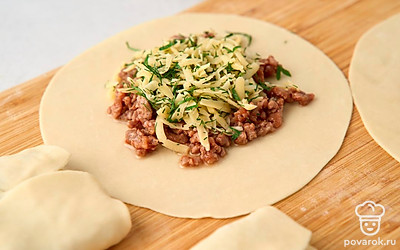 Распределите по получившимся лепешкам начинку из фарша, выкладывая ее в центр. Слегка размажьте начинку, придав ей форму прямоугольника. Укройте слой фарша слоем сыра с зеленью. Сверните лепешки конвертами с начинкой внутри.