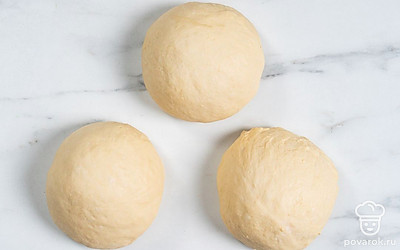 Немного обомните поднявшееся тесто руками и разделите на три равные части. Из каждой части сформируйте небольшой шар, положите на стол на расстоянии друг от друга. Накройте пищевой пленкой и оставьте на 15 минут.