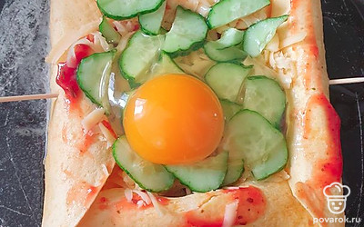 Добавляем мелко нарезанные огурчики, разбиваем сверху яйцо. Выкладываем в сковородку. Добавляем водичку и держим под крышкой 5-7 минут до готовности яйца.