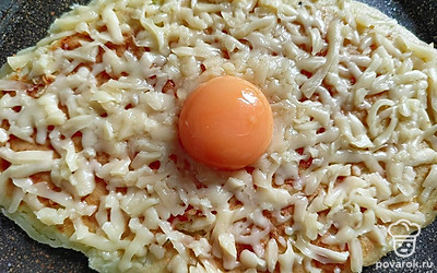 Переверните на другую сторону. Через 2 минуты посыпьте хачапури сыром (40 граммов). В центр выложите яичный желток. Готовьте под закрытой крышкой 3-4 минуты на небольшом огне.