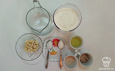 Воду налейте в кувшин. Муку поместите в миску. Миндаль и семечки высыпьте в пиалу. Сахарный песок, дрожжи, соль поместите в блюдца.