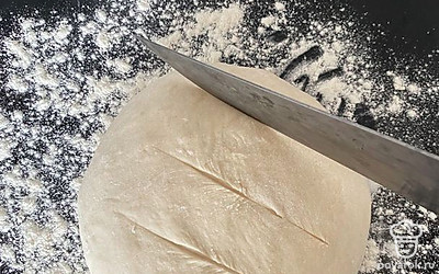 Спустя 30 минут обмять тесто, выложить на противень, присыпанный мукой, сформировать будущий хлеб и сделать неглубокие насечки ножом.