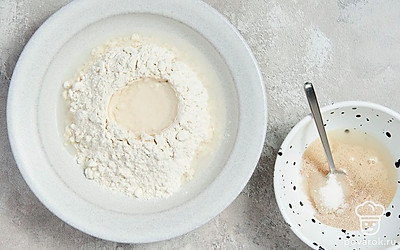 Приготовьте опару. В миску влейте 2 ст. л. теплой воды, добавьте сахар, дрожжи и хорошо перемешайте. Полученную смесь оставьте на 15 минут. Затем в отдельную миску всыпьте муку, добавьте к ней оставшуюся воду и опару, тщательно перемешайте. Накройте миску полотенцем и уберите ее в теплое место на 8-10 часов.