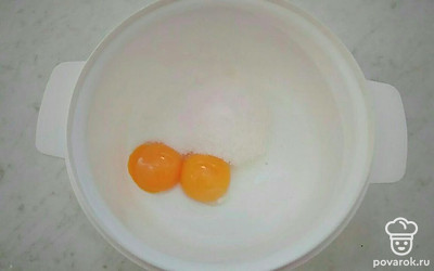 В глубокой миске соедините куриные желтки, сахар и ванильный сахар и взбейте массу миксером до пышной белой массы. Присоедините к яично-сахарной смеси размягченное сливочное масло и продолжайте взбивать смесь. Затем влейте к ней теплое молоко, добавьте муку и разрыхлитель и тщательно вымешивайте тесто до гладкости и однородности.