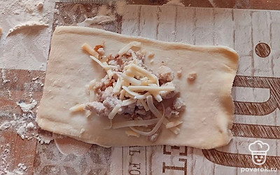 Слоеное тесто раскатайте, разрежьте на квадраты. На каждый квадрат выложите ложку куриного фарша и немного твердого сыра. Скрепите углы пирожка, смажьте каждый яйцом.