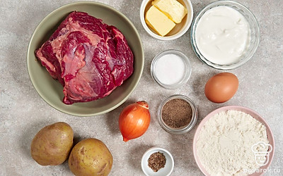 Просейте муку через мелкое сито. Помойте куриное яйцо. Заранее достаньте из холодильника сливочное масло, чтобы оно стало мягким. Разморозьте, промойте и обсушите говядину. Помойте и очистите лук и картофель. Разогрейте духовку до 180°С. Застелите противень пергаментом.