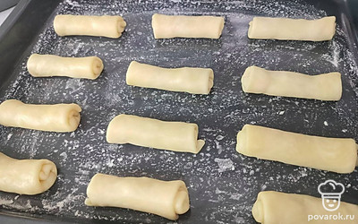 Вдоль узкого края пласта выложите начинку, накройте узким краем, затем накройте боковыми краями. И затем сверните в трубочку. Выложите пирожки на присыпанный мукой противень. По желанию можно смазать пирожки взбитым яйцом.