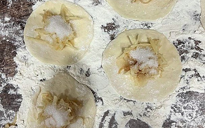 На раскатанное тесто выкладываем предварительно натертое яблоко. Добавляем 1,5 чайной ложки сахара.