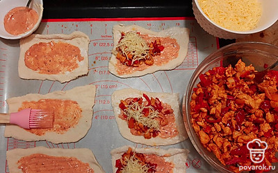 Раскатываем тесто и режем на полоски нужного размера. Чем шире полоска, тем больше размером пирожок. Смешиваем кетчуп с майонезом и смазываем каждую полоску, выкладываем начинку из курицы и перца и посыпаем сверху натертым сыром. 