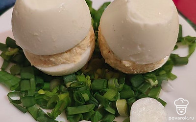 Соединить половинки так, чтобы получилось целое яйцо. Ножом срезать дно яйца, чтобы можно было его поставить. Срезать верхушку яйца, чтобы разместить шляпки из помидора. Зеленый лук нарезать колечками и выложить на тарелку. Яйца поставить на эту подушку из лука. 