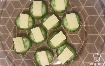 Сыр нарежьте на небольшие ломтики и выложите поверх огурцов.