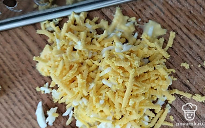 Натираем вареное куриное яйцо. Одну часть добавляем в тарелку, а вторую часть оставляем для украшения.