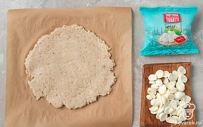 Нарежьте моцареллу тонкими ломтиками. Смочите пергаментную бумагу на столе небольшим количеством воды. Мокрыми руками выложите на пергамент половину курино-овсяной массы, придайте ей форму плоской лепешки.