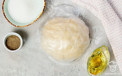 Приготовьте тесто. В глубокой емкости соедините муку и соль. В муке сделайте ямку, налейте в нее растительное масло и воду. Замесите тесто сначала в миске, а потом выложите его на твердую поверхность и продолжите вымешивать. Тесто должно получиться эластичным, без комочков. Сформируйте из теста шар, накройте полотенцем на 30 минут, чтобы оно подошло.