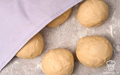 Скатайте из теста объемную колбаску и разделите ее на 6 равных по размеру частей. Придайте кусочкам теста форму шариков. Прикройте шарики полотенцем и оставьте на 8-10 минут.