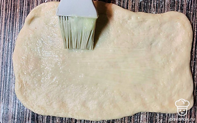 Отрежьте кусочек теста, раскатайте его в большой прямоугольник. Смажьте всю поверхность растопленным сливочным маслом. 