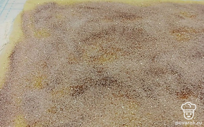 Тесто обминаем, раскатываем в пласт и смазываем 70 граммами сливочного масла. Сахар смешиваем с корицей и распределяем по тесту.