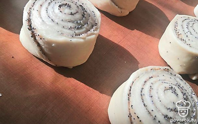 Берём острый нож и нарезаем рулетик на 12 частей. Край подворачиваем под булочку. И ставим на противень на расстоянии друг к другу. Накрываем пищевой плёнкой и даём расстояться минут 40.