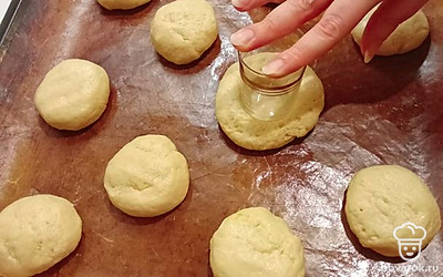 Тесто разделите на 10 одинаковых шариков и выложите их на противень, покрытый пергаментом или антипригарным ковриком. С помощью рюмки или руками в каждом шарике сделайте углубление. Яйцом смажьте края каждой плюшки. В углубление выложите джем. 