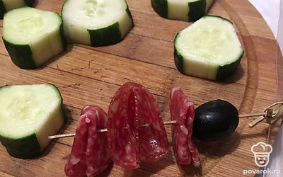 На шпажку нанизываем маслину и 3 листочка сырокопченой колбасы, сложенных четвертинками. Разворачиваем края в разные стороны елочкой.