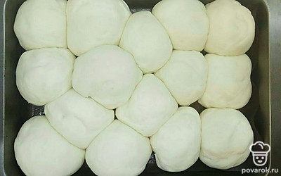 Когда все булочки сформированы выложите их в форму для выпечки, предварительно смазав ее небольшим количеством растительного масла или любого кулинарного жира. Накройте полотенцем или пищевой пленкой и оставьте в тепле на 40 минут. Поднявшиеся булочки смажьте небольшим количеством воды и отправьте в разогретую духовку до 180 °C для выпекания на 30 – 35 минут.