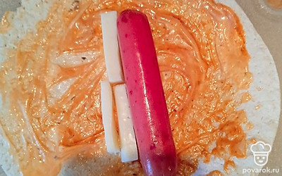 На круглый лаваш выкладываем одну чайную ложку кетчупа и одну чайную ложку майонеза, размазываем по всему лавашу. Кладем сосику. Рядом выкладываем сыр. 