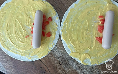 Помидор нарежьте кубиком, выложите полоской на тортилью. Сверху разложите сосиски.