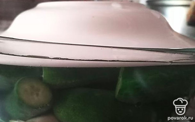 В емкость с зеленью добавить чеснок, огурцы, залить горячим рассолом, положить сверху гнет. Когда остынет, убрать на сутки в холодильник. 